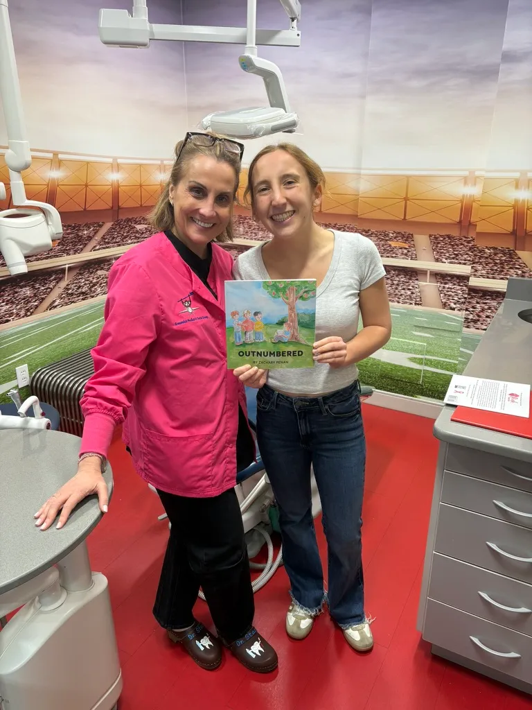 Dr. Stacy and a member of the Outnumbered team holding a copy of the Outnumbered book at Greenwich Pediatric Dental Group, LLC.